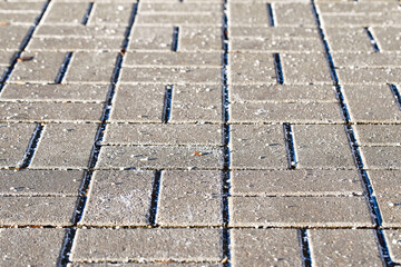 Wintertime deicing with salt crystals on textured paving stone slabs, surface treatment for icy conditions and enhancing pedestrian safety. Scattering of salt crystals on paving stone slabs in winter