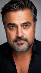 Obraz premium Portrait of a middle-aged man with dark hair and a beard, against a neutral background.