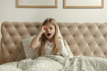 A sleepy little girl lies in bed and yawns. 
