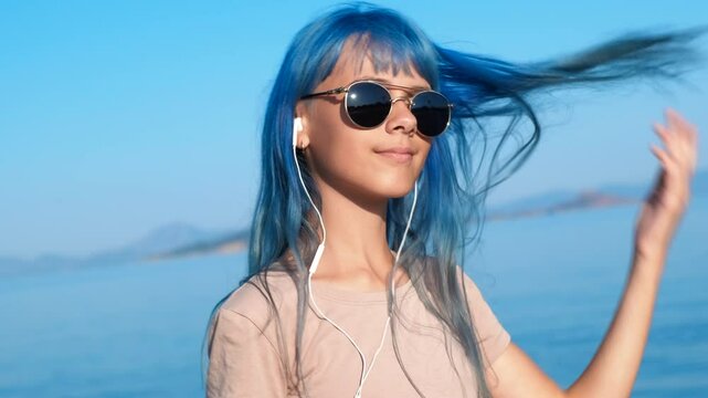 Girl in earphones mooving by sea. A modern dancing teen in headphones relax the vacation time on the beach in sun rays.