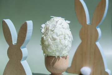 Wooden minimalism low-key bunny decor. Easter egg made of white lilac spring flowers in pastel...