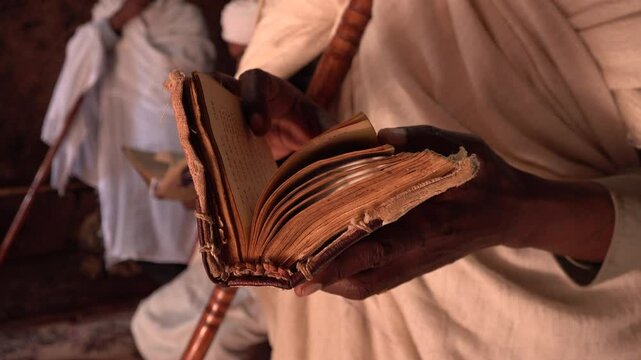 Priest reads and sings verses from historic Amharic Bible book inside rock-hewn Church of Saint George in Lalibela, ancient civilization and peaceful atmosphere in Ethiopia Africa

