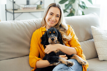 Cheerful caucasian charming woman in a casual wear, sitting on a soft couch in a living room,...