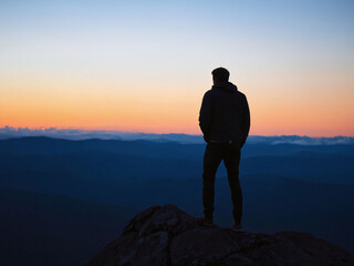Man gazes at a colorful sunset from a mountain peak overlooking valleys and distant hills