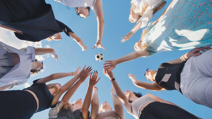High school students reaching for a soccer ball under a summer sky