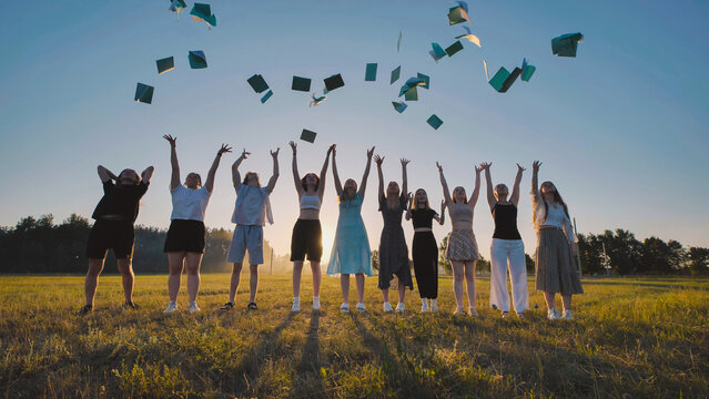 High school students joyfully tossing books in the air to celebrate the end of the school year in a field at sunset