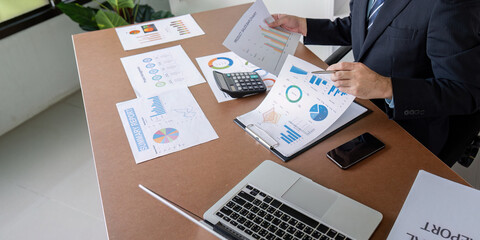 Financial analyst reviewing charts and graphs from reports in a modern office setting.