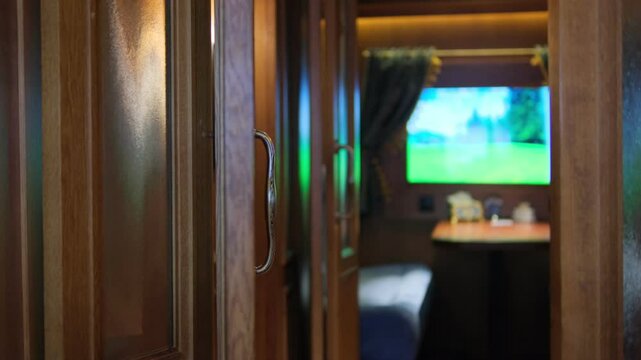 A nostalgic train compartment featuring wooden doors, a cozy bed, a small table, and a window displaying a moving green landscape, evoking a sense of travel