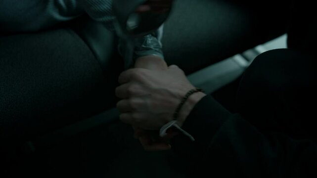 Closeup handheld shot of anonymous criminal tying up hands of female hostage using duct tape, immobilizing victim while transporting her in car, human abduction and trafficking