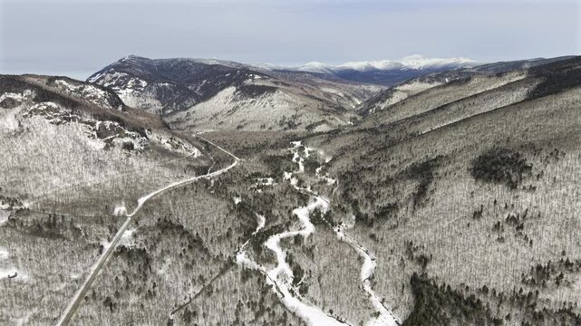 Aerial HDR drone footage of White Mountains in New Hampshire near Crawford Notch on a winter day with RT 302 carving through the snowy landscape