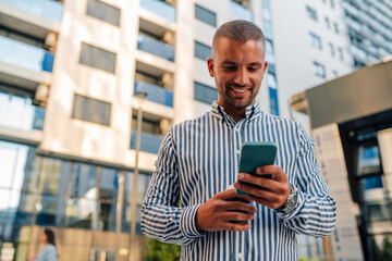 Young manager smiling and texting on phone in front of office building