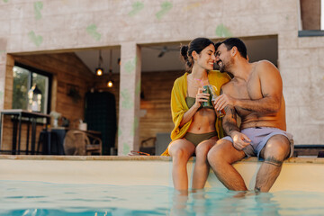 Happy couple relaxing by the pool with refreshing drinks in summer