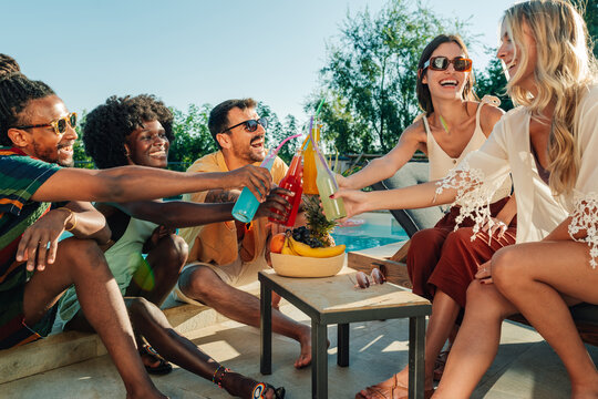 Friends toasting colorful drinks at poolside party