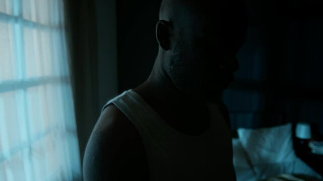 Close-up shot of African American man sleepwalking around his bedroom in dark with his eyes closed