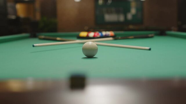 No people shot of white cue ball placed on baize table together with two cue sticks and billiard balls prepared for pool game in club