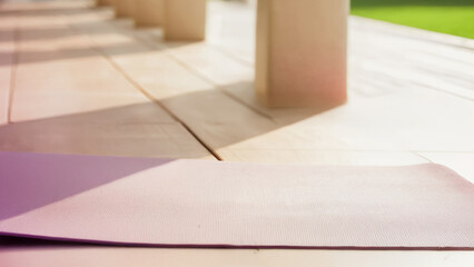 A comfortable yoga mat spread out on a wooden deck, the bright sun gently enveloping the resting place, symbolizing relaxation, solo practice, fitness and tranquility in an outdoor wellness atmosphere