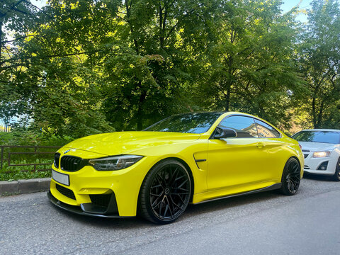 A yellow BMW F82 M4 competition on a country road in summer. BMW M4 F82 coupe in custom wide body kit with carbon fiber parts and front spoiler. German cars. 