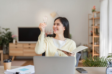 Cheerful woman celebrating a bright idea with a light bulb in her home office