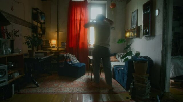 Full shot of restless and anxious man in undershirt and jeans wandering around shabby room, reading letters or draft of novel and throwing papers away, feeling apathetic and hopeless