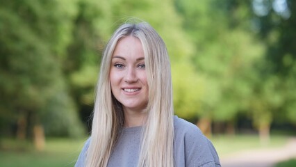 Obraz premium A cheerful young woman with flowing hair is posing joyfully in a vibrant and lush green park, radiating happiness