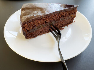 Delicious slice of rich chocolate cake on white plate with fork