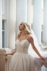 Blonde bride with veil and wedding dress posing on balcony.
