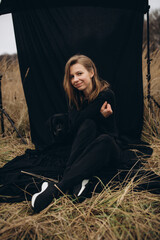 Obraz premium beautiful woman dressed in black pants and sweater sits on a black background with a beautiful black Labrador dog. Labrador Retriever dog