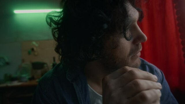 Closeup of unhappy Caucasian man with stubble indifferently looking out window, sitting alone in kitchen and thinking of problems in life