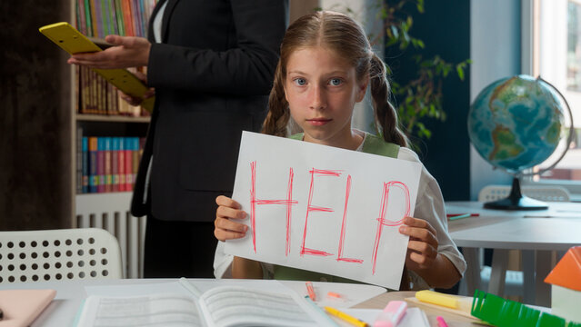 Strict angry Caucasian teacher professor walking around little sad helpless girl kid schoolgirl school child pupil student learner punishment show to camera paper write asking help need in classroom