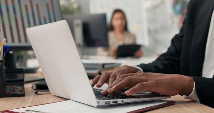 Close-up of silver latop standing on wooden desk, dark-skinned man working on it, young hands, typing text into keyboard, tapping fingers on computer