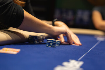 A close up view of a poker game in progress, showing a player's hands reaching for blue and white chips on a blue felt table with a card visible.