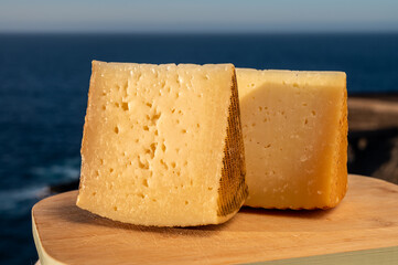 Assortment of Spanish hard cheeses, curado, manchego, goat cheese served outdoor with blue sea on background, close up