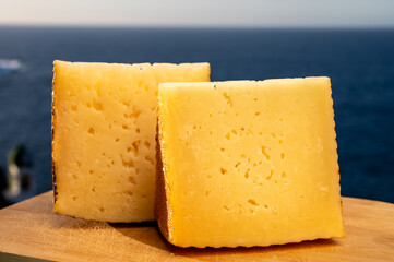 Assortment of Spanish hard cheeses, curado, manchego, goat cheese served outdoor with blue sea on background, close up