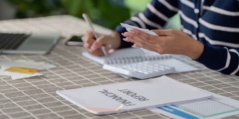 Individual reviewing financial report and planning bills while using a calculator and taking notes...