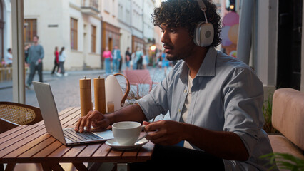 Indian Arabian man male businessman client business guy online work in cafe distant education using devices laptop phone listen music in headphones outdoors tourist traveler customer drink coffee city
