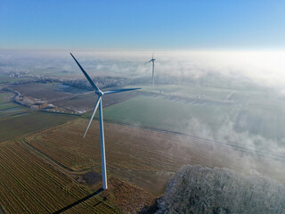 Aerial view of wind turbines in a winter landscape with sun and deep fog over the fields, wind energy, renewable energies, energy transition, climate protection