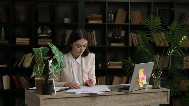 Woman works at an office table at the computer and makes notes in documents. Business woman works on an important and complex project and yawns from fatigue. Dedication and continuous work