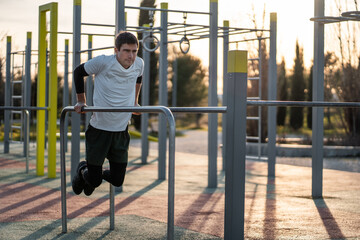 young athletic man exercising fitness calisthenics workout and making dips at street gym during...