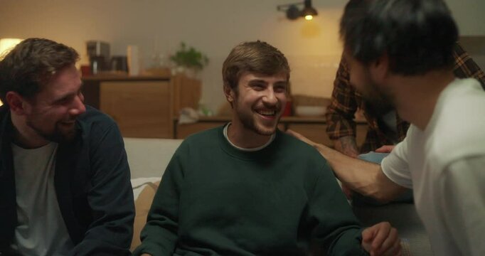 Happy cheerful guy tells a story to his friends and they laugh on the sofa during a bachelor party in the evening