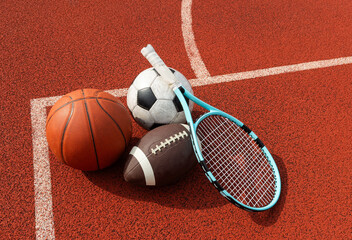 A variety of sports equipment including an american football, a soccer ball, a tennis racket, a tennis ball, and a basketball