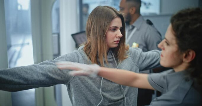 Security Checkpoint in Airport Terminal: Female Security Officer Inspects Young Woman Body for Suspicious Items After Metal Detector Scanning Gates. TSA Screening Procedures. Tourist Going on Trip.