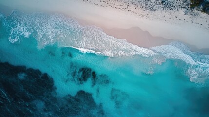 A stunning aerial view of the sea, deep blue waves blending into soft turquoise near the shore.