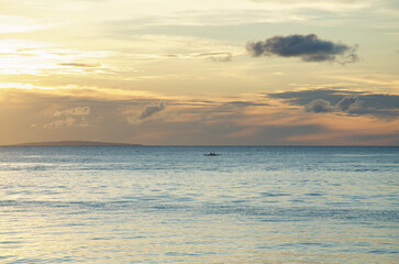 Obraz premium A tranquil seascape at Boracay Island, with a lone boat on calm waters under a dramatic sky, capturing the serene beauty of the horizon and the golden hues of sunset.