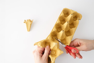 A pair of hands using scissors to cut a yellow egg carton. Step in creative process, top view. DIY...