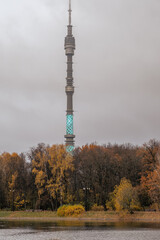 Obraz premium Tower surrounded by autumn trees near the water in a cloudy setting showcasing illumination in the evening sky