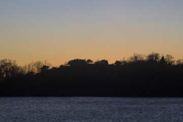 Sunset in yellow tones with backlit trees on a blue lake in horizontal © MiguelA