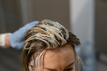 Naklejka premium Hair coloring process with a stylist applying bleach to a clients roots in a modern salon setting