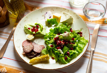 Set of traditional Albanian appetizers of fresh green salad with soft goat cheese and pomegranate, piquant stuffed pepper, quail egg, yogurt sauce, sliced smoked sausage and cheeses served on plate..