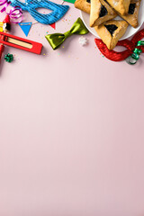 Purim celebration vertical background with colorful masks, hamantaschen cookies, noisemakers, and festive decorations on a pastel pink backdrop.v