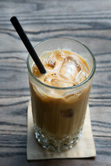 A close-up of an iced latte served in a glass with ice cubes and a straw, placed on a wooden table, highlighting its refreshing and creamy texture
